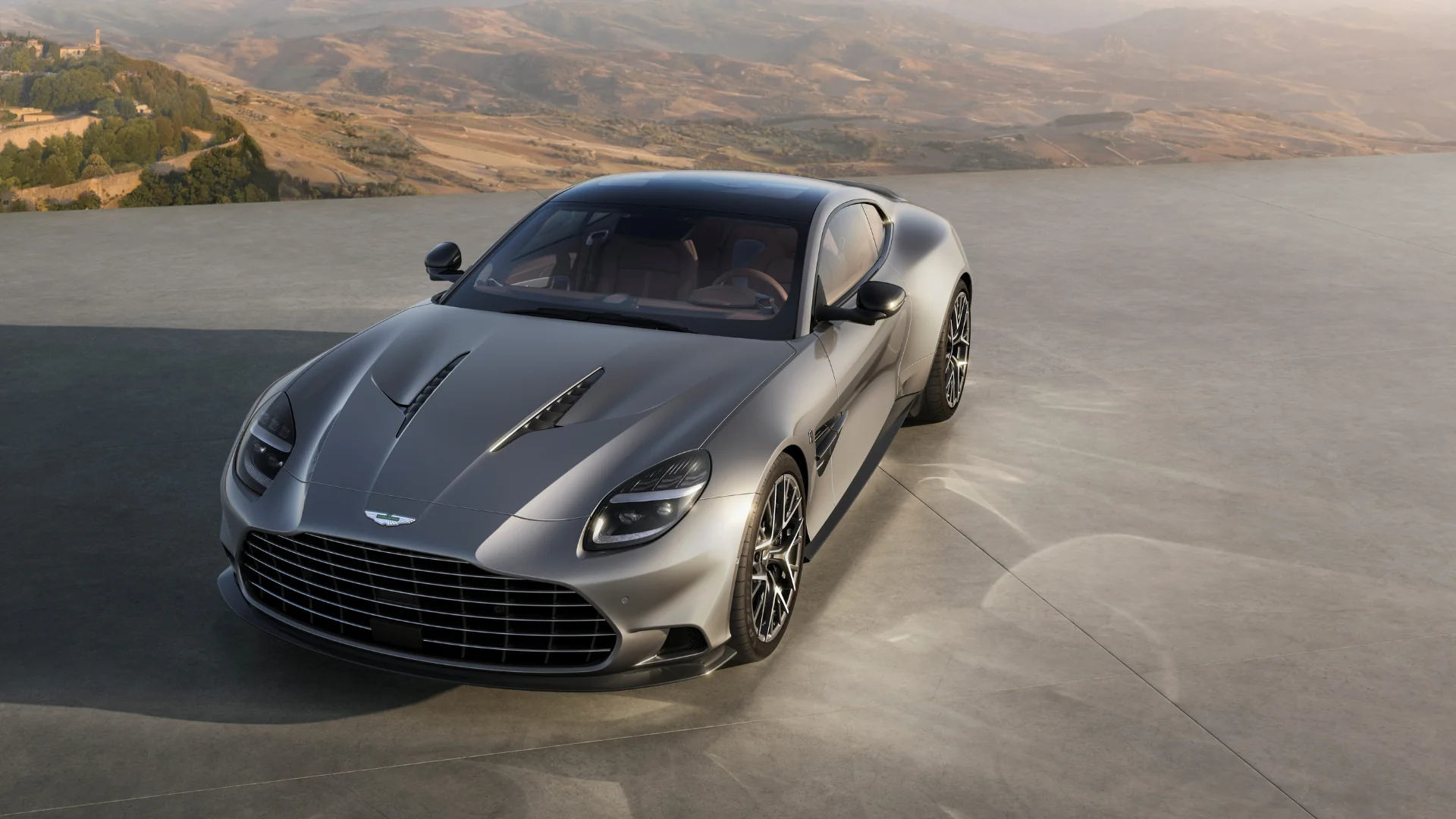 Silver Aston Martin sports car with a mountain backdrop.