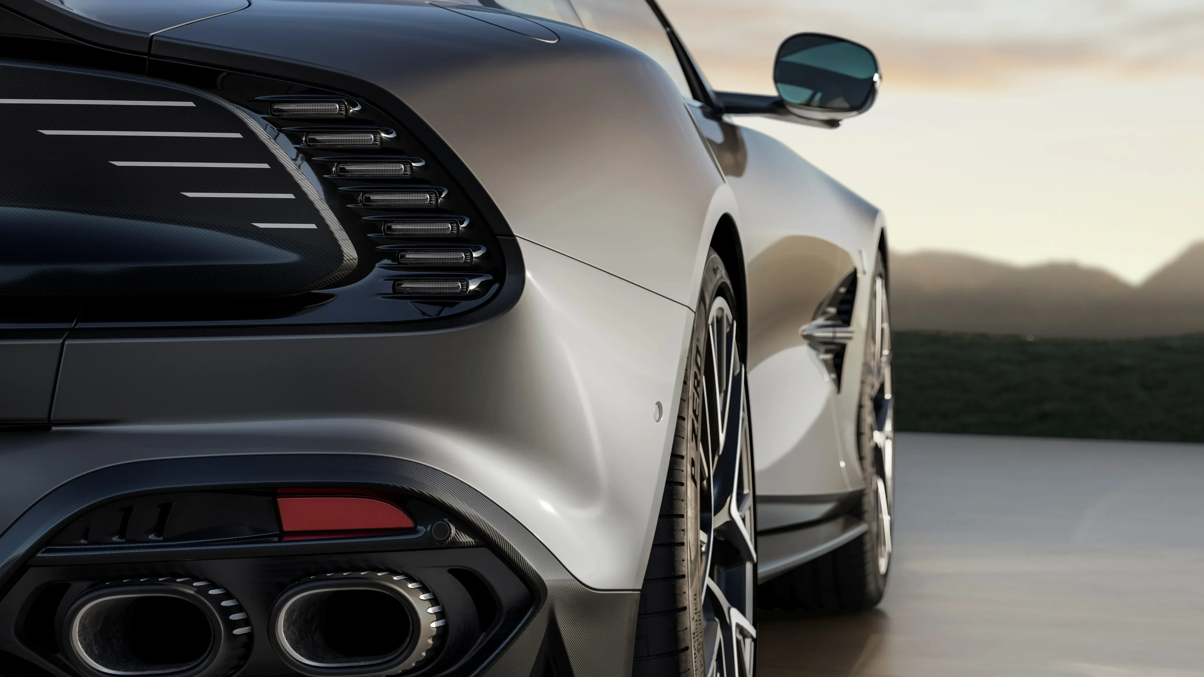 Rear view of a silver Aston Martin Vanquish showing taillights, quad exhaust pipes, and side profile.