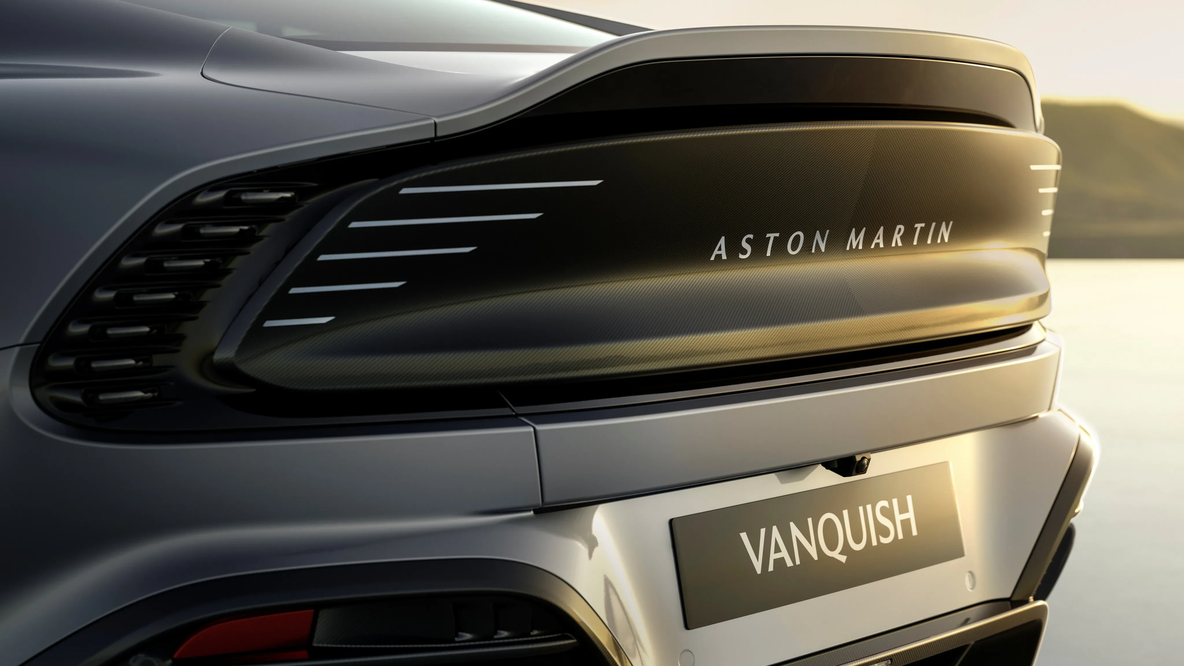 Rear design of a silver Aston Martin Vanquish featuring modern LED taillights and Vanquish license plate.
