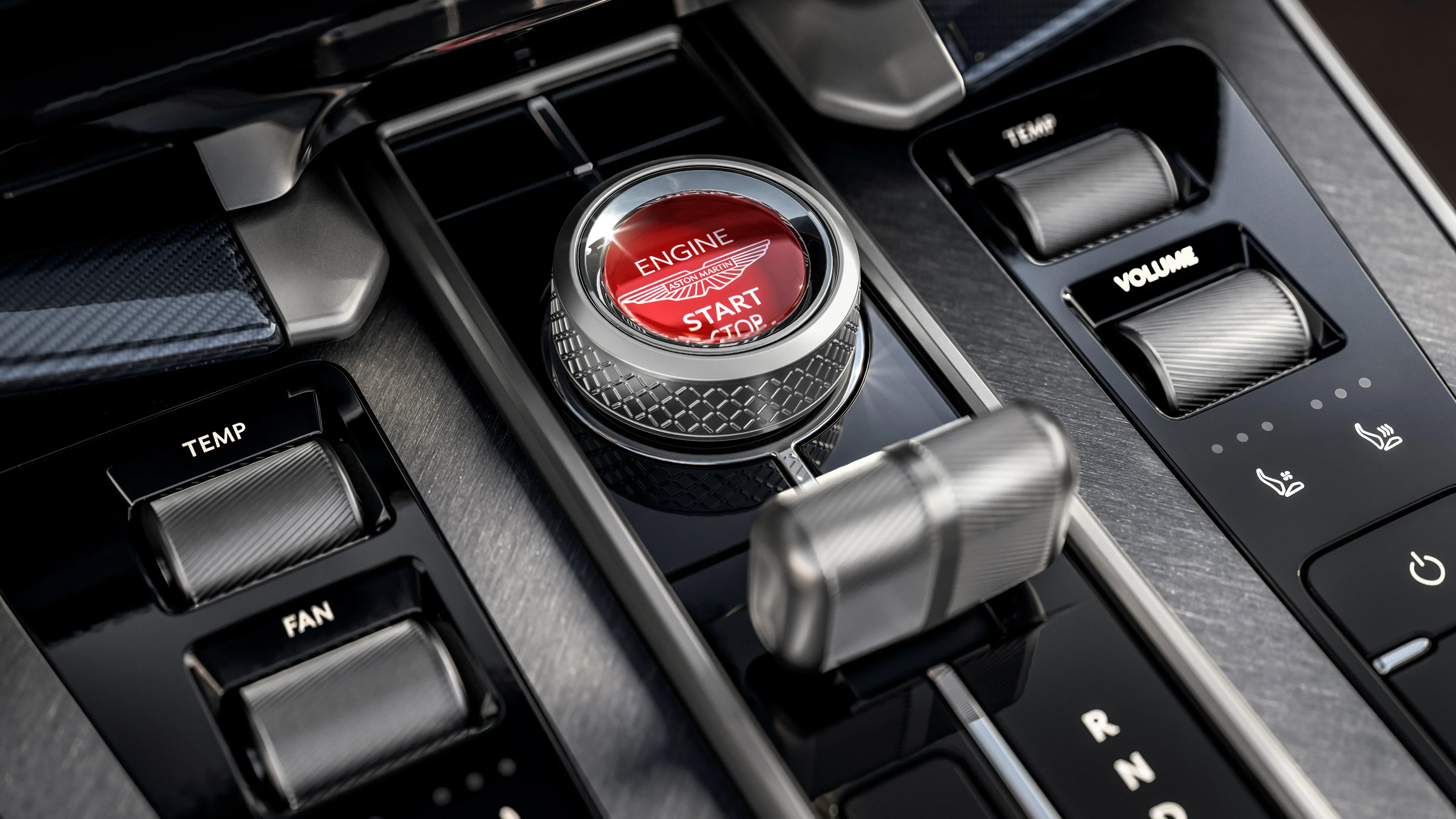 Center console of an Aston Martin Vanquish featuring a glass engine start-stop button and metallic controls.