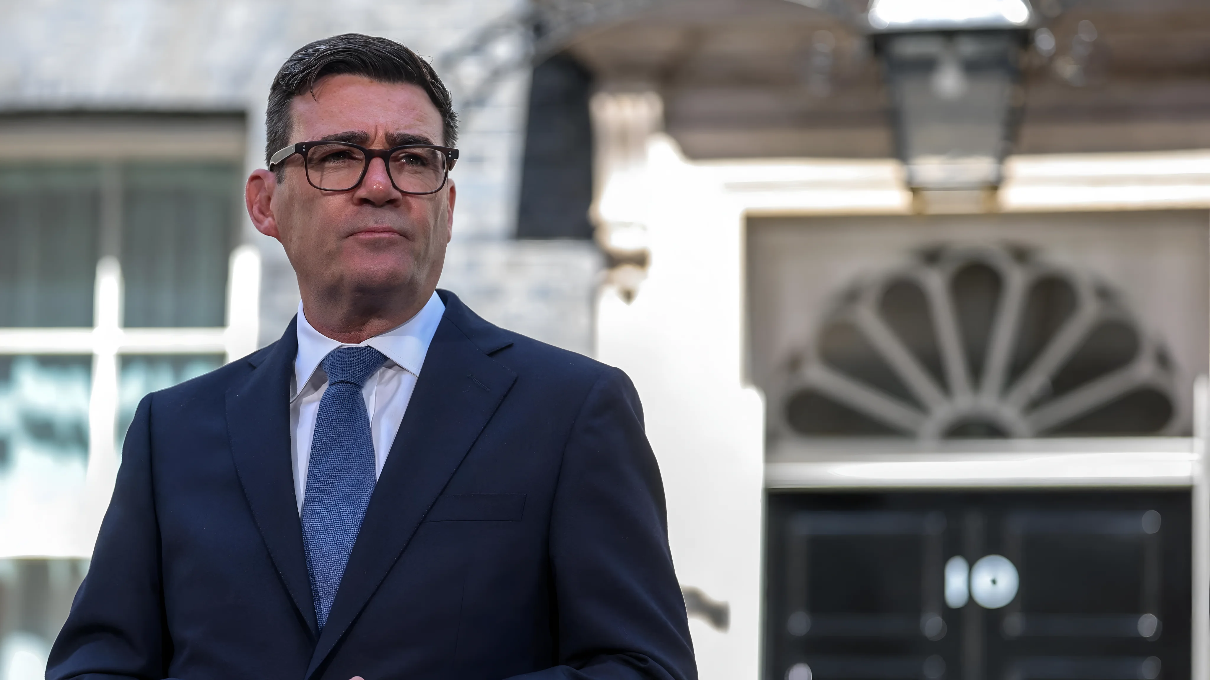 Andy Burnham stands in front of 10 Downing Street wearing a dark suit and blue tie. Credit: BBC / Getty Images.