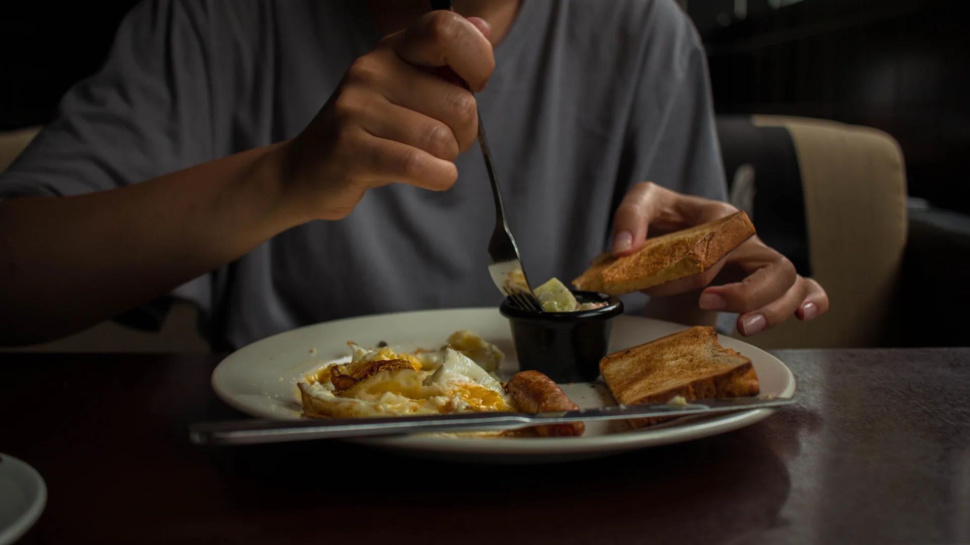 A person is enjoying breakfast of eggs and toast at home in a cozy setting. Credit: Sergey Meshkov.
