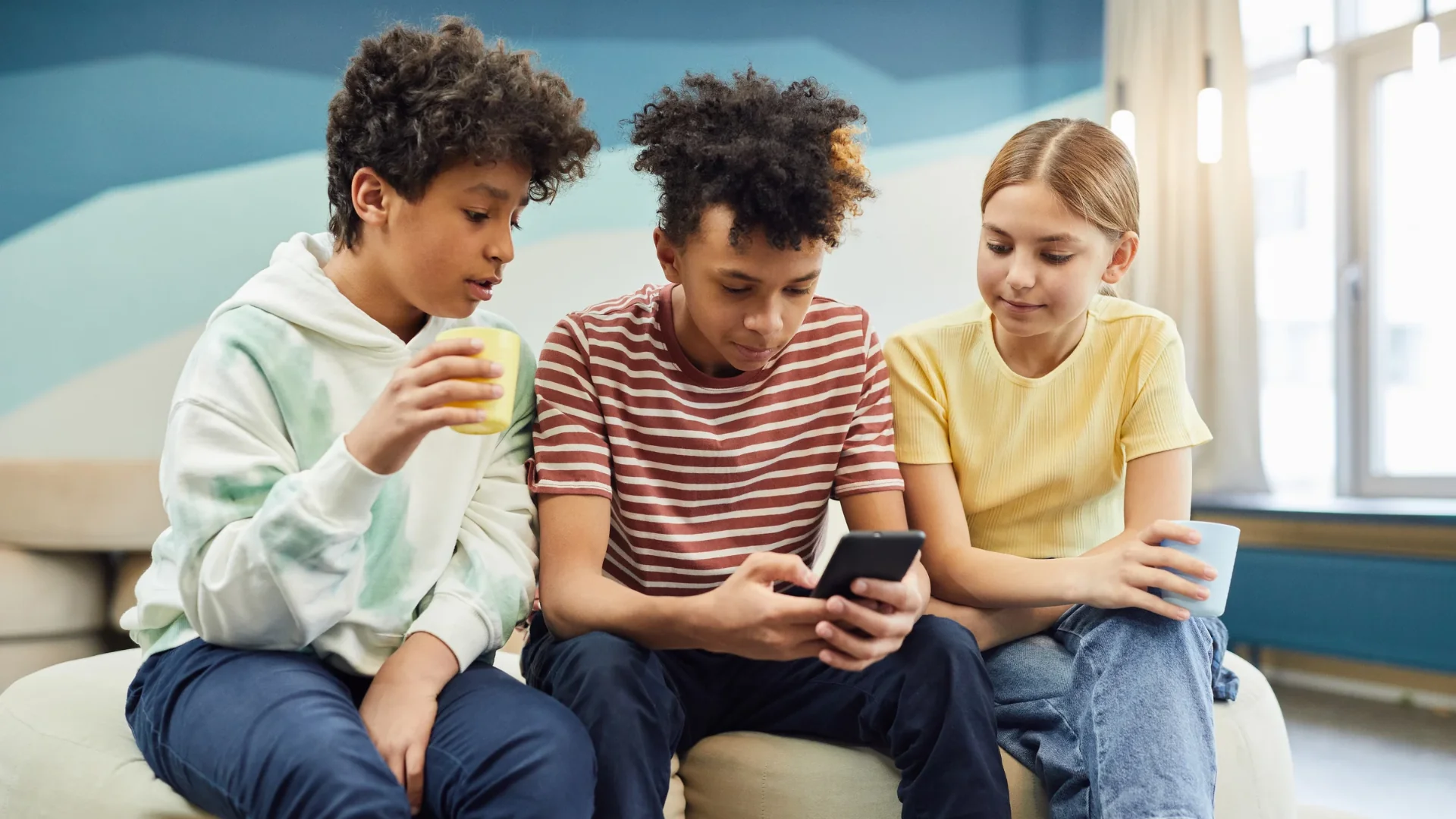 Three young people relax indoors, enjoying their free time and browsing their smartphones together. Photo: Vanessa Lorin