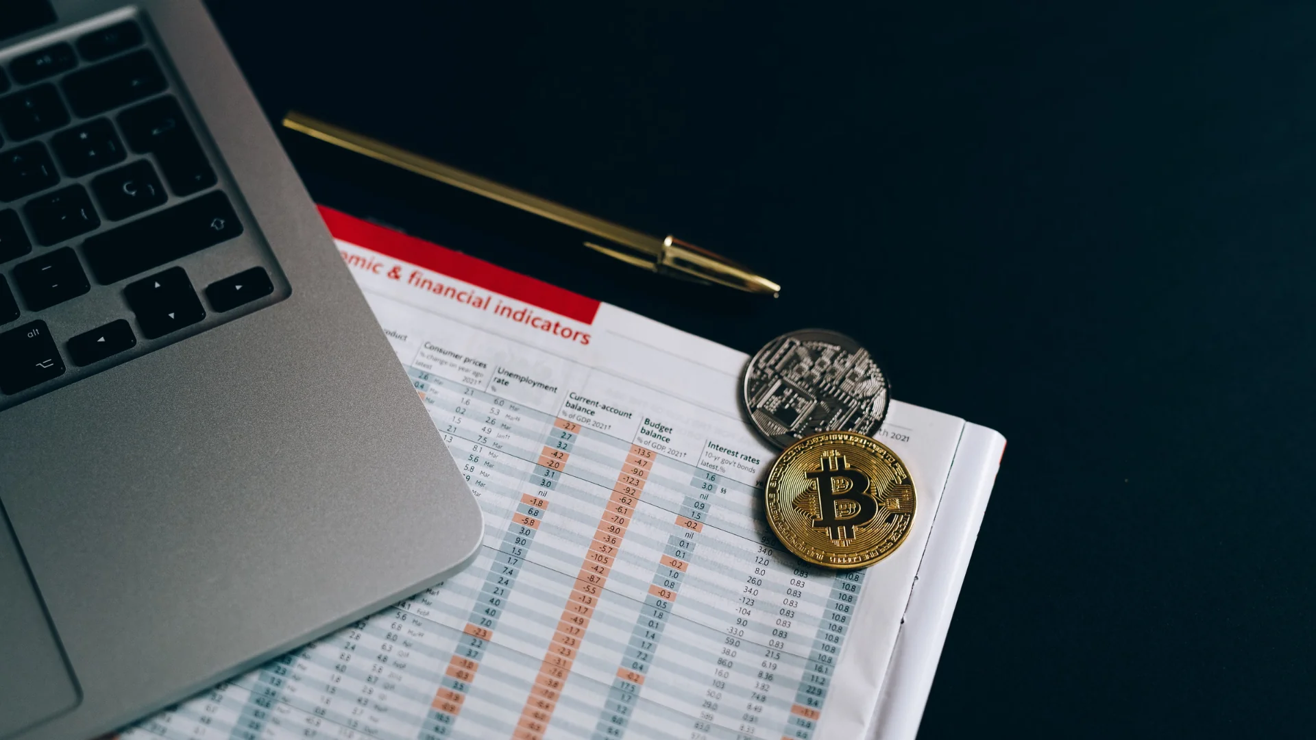 Bitcoin and cryptocurrency coins on a financial document next to a laptop. Photo: Leeloo The First.