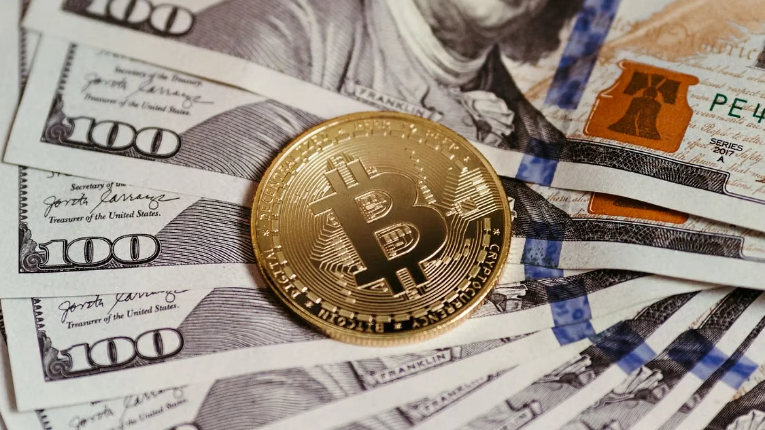 A gold Bitcoin coin resting on US dollar bills, symbolizing digital and fiat currency. Photo: Jonathan Borba.