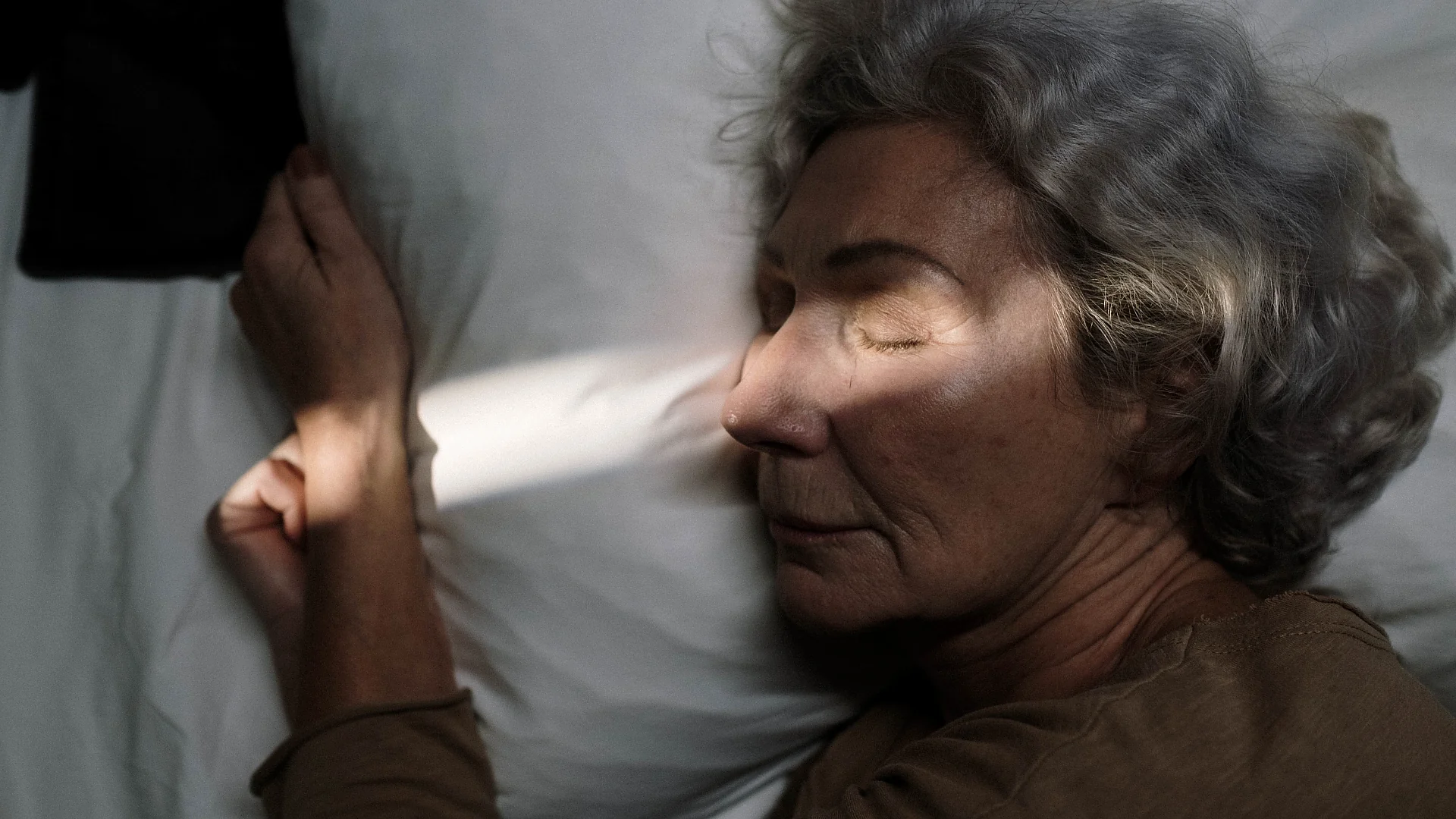 An elderly woman resting peacefully on a pillow with soft sunlight illuminating her face. Photo: Ron Lach.