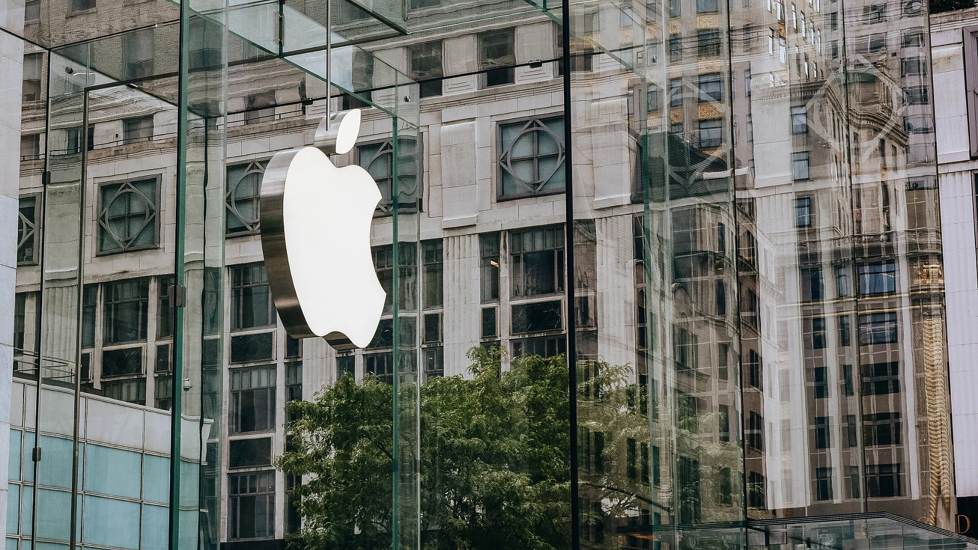 Apple logo displayed on a modern glass facade with urban reflections. Photo: Tim Gouw.